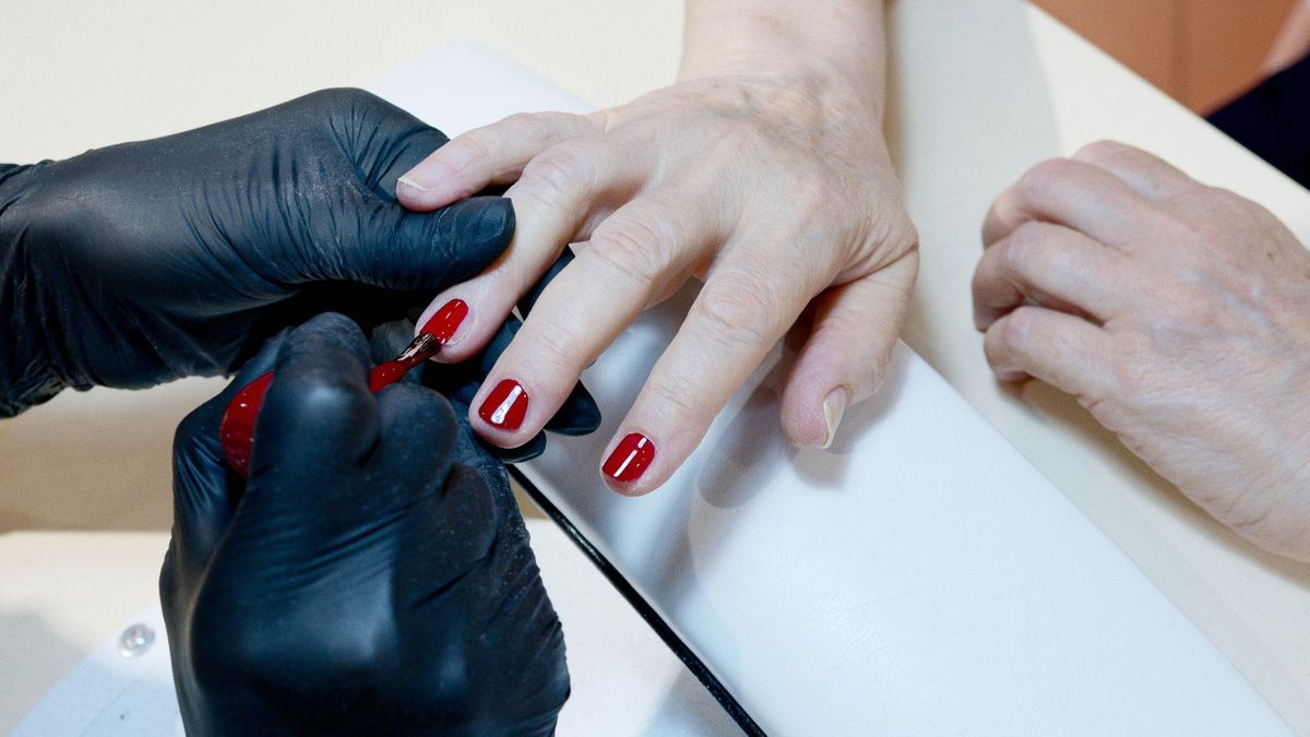 Voorbeeld: nagelstyliste met zwarte handschoenen lakt nagels rood